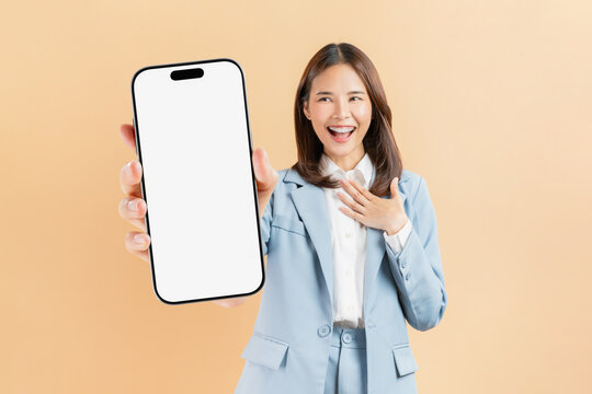 Confident Asian businesswoman holding big smartphone mockup of blank screen and smiling on beige color background.
