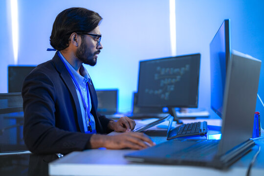 Focused Indian male AI developer coding a complex machine learning algorithm late at night. A dedicated data scientist working on a neural network at a multi-monitor workstation.