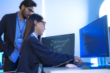 Asian female AI programmer and Indian male data analyst reviewing code on a monitor. Diverse tech...