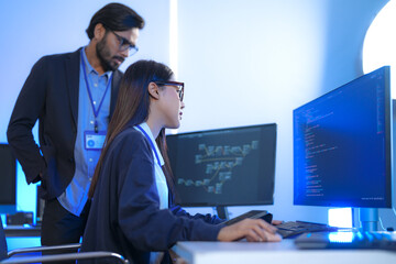 Asian female AI programmer and Indian male data analyst reviewing code on a monitor. Diverse tech...