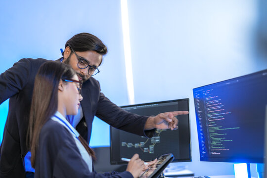 Asian female AI programmer and Indian male data analyst reviewing code on a monitor. Diverse tech professionals collaborating on an artificial intelligence project in a modern office. - Powered by Adobe