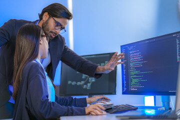 Asian female AI programmer and Indian male data analyst reviewing code on a monitor. Diverse tech...