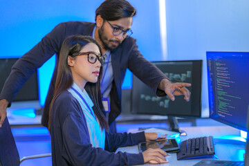 Asian female AI programmer and Indian male data analyst reviewing code on a monitor. Diverse tech...