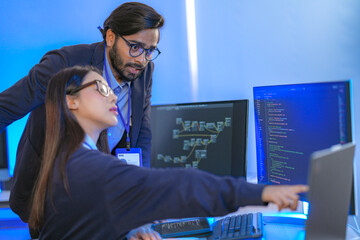 Asian female AI programmer and Indian male data analyst reviewing code on a monitor. Diverse tech...