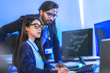 Asian female AI programmer and Indian male data analyst reviewing code on a monitor. Diverse tech...