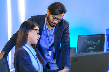 Asian female AI programmer and Indian male data analyst reviewing code on a monitor. Diverse tech...