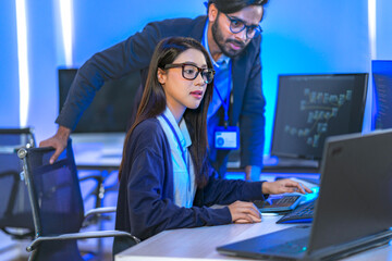 Asian female AI programmer and Indian male data analyst reviewing code on a monitor. Diverse tech...