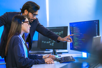 Asian female AI programmer and Indian male data analyst reviewing code on a monitor. Diverse tech...