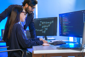 Asian female AI programmer and Indian male data analyst reviewing code on a monitor. Diverse tech...