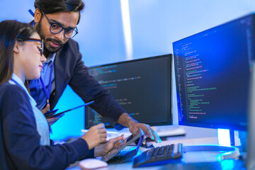 Asian female AI programmer and Indian male data analyst reviewing code on a monitor. Diverse tech...