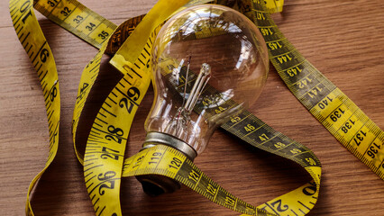 Light Bulb and Measuring Tape on Wooden Table