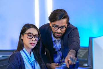 Asian female AI programmer and Indian male data analyst reviewing code on a monitor. Diverse tech...