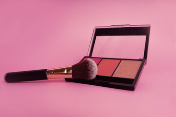 Cosmetic brush resting beside blush palette on pink background creating an elegant beauty...