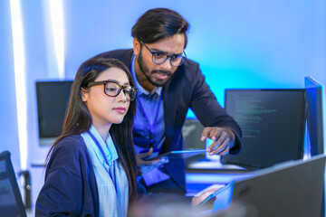 Asian female AI programmer and Indian male data analyst reviewing code on a monitor. Diverse tech...
