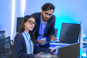 Asian female AI programmer and Indian male data analyst reviewing code on a monitor. Diverse tech...