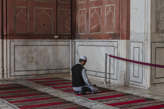 New Delhi, India - 24 June 2025: View of a man praying inside the Jama Masjid, its red sandstone walls contrasting with the cool marble interiors.