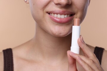 Young woman with lip balm on beige background, closeup