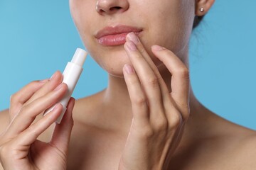 Young woman with lip balm on light blue background, closeup