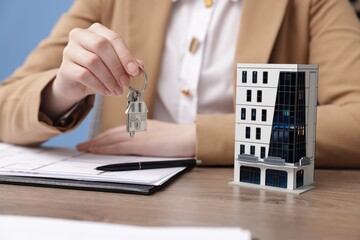 Real estate agent holding key and house model at desk in office, closeup