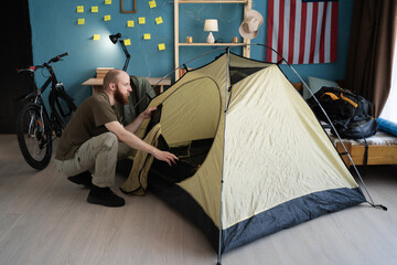 Preparing for a hike in the mountains. Packing a tent for camping at home. Bearded man hiker...