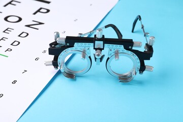 Vision test chart and trial frame on light blue background, closeup