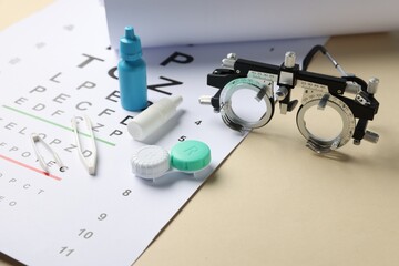 Vision test chart, trial frame, lenses, tweezers and bottles of medical drops on beige background,...