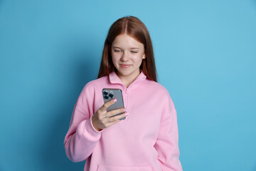 Beautiful teenage girl using smartphone on light blue background