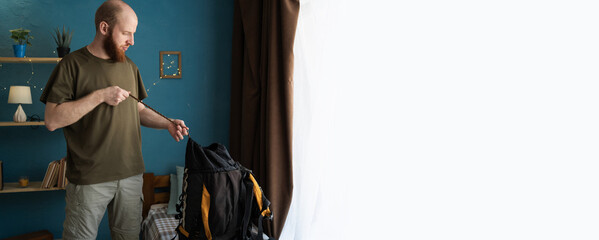 Young bearded man traveler prepare for hiking vacation in the living room at home. backpacker travel concept