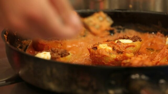 Chef stirs seasoned minced meat. Stuffed pasta shells with meat filling simmer in bubbling tomato sauce. This hearty, delicious Italian meal is perfect for a family dinner.