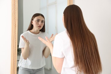 Beautiful woman looking at herself in mirror indoors