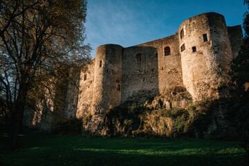 Old stone castle with round towers on a grassy hill under a blue sky