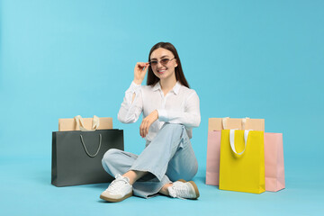 Positive woman with shopping bags on light blue background