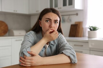 Scared woman suffering from paranoia at table in kitchen