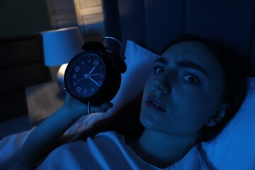 Frustrated woman with alarm clock suffering from insomnia in bed at home