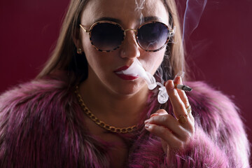 Beautiful woman in fur coat smoking cigarette on dark pink background, closeup