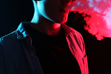 Man using electronic smoking device in neon lights on black background, closeup