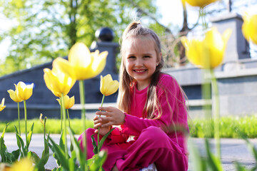 Cute little girl near beautiful yellow tulips outdoors