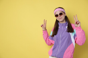 Teenage girl in sunglasses showing peace sign on yellow background, space for text