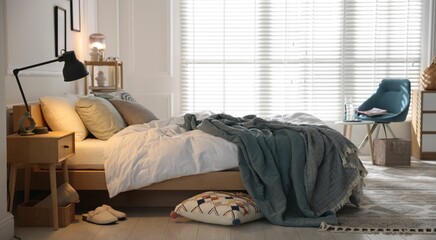 Cozy bed with soft linens, nightstand and lamp in stylish room. Home textile