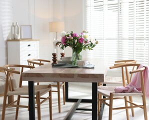 Dining table with beautiful flowers and dishware in room. Interior design