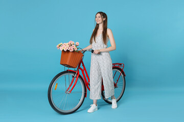 Smiling woman and bicycle with basket of flowers against light blue background