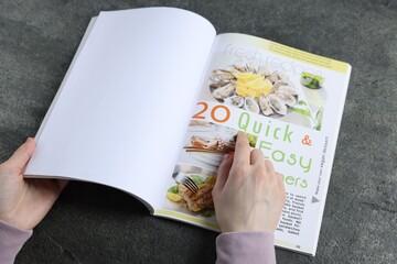 Woman reading magazine at grey table, closeup. Mockup for design