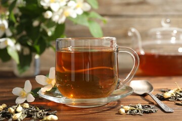 Aromatic jasmine tea in glass cup, brew and flowers on wooden table, closeup
