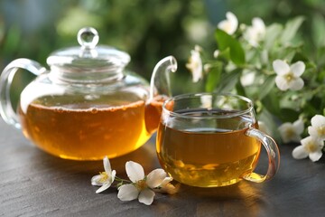Tasty jasmine tea in cup, teapot and flowers on black table, closeup