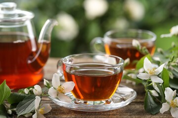 Tasty jasmine tea in cups, teapot and flowers on wooden table, closeup