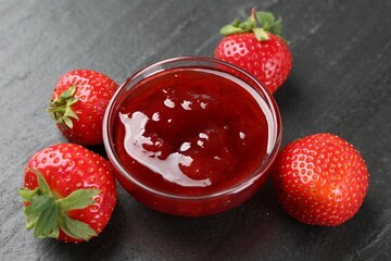 Tasty homemade strawberry jam and berries on black table, closeup