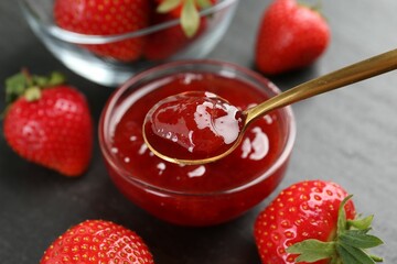 Taking tasty homemade strawberry jam with spoon at black table, closeup