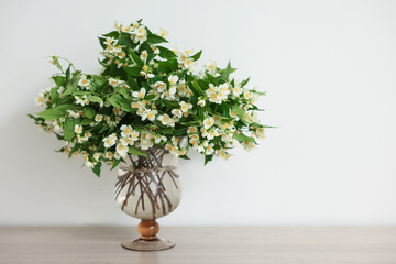 Beautiful jasmine flowers in vase on wooden table indoors, space for text