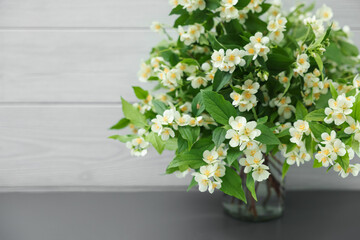 Beautiful jasmine flowers in vase on grey table near white wooden wall indoors, closeup. Space for text