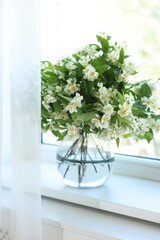 Beautiful jasmine flowers in vase near window indoors